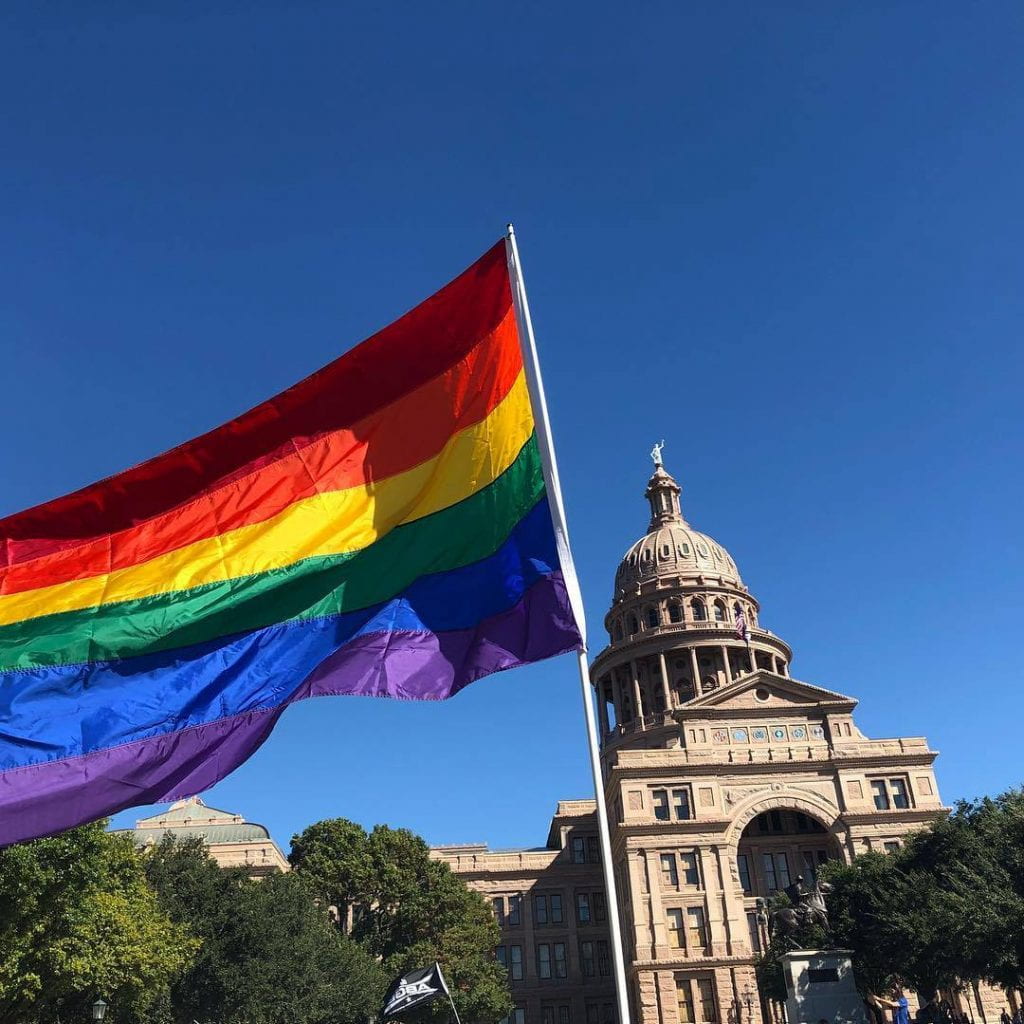 Photo of rainbow pride flag in front of the Texas state capitol