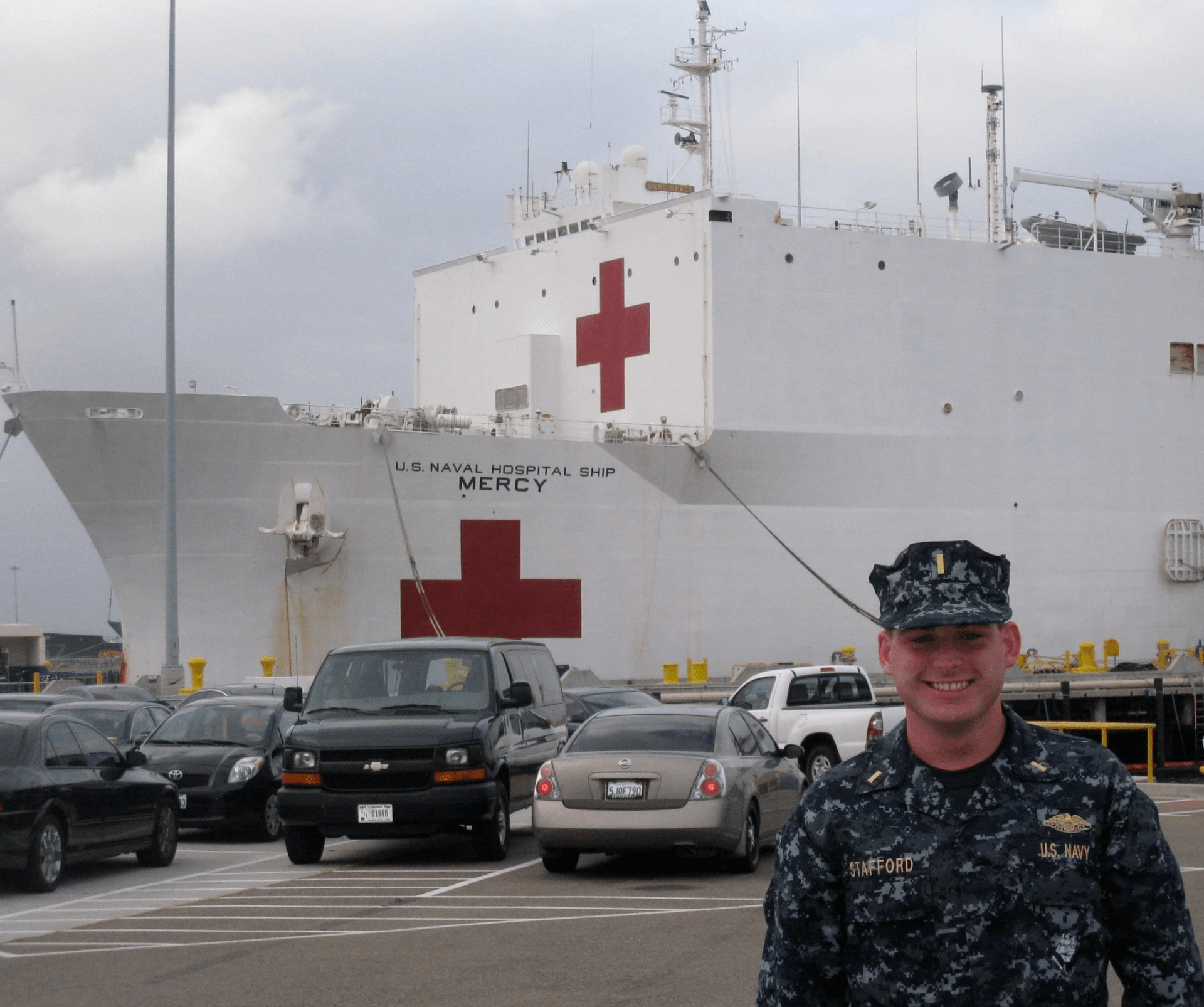 Photo of chris in his navy uniform standing outside of a navy hospital ship. 