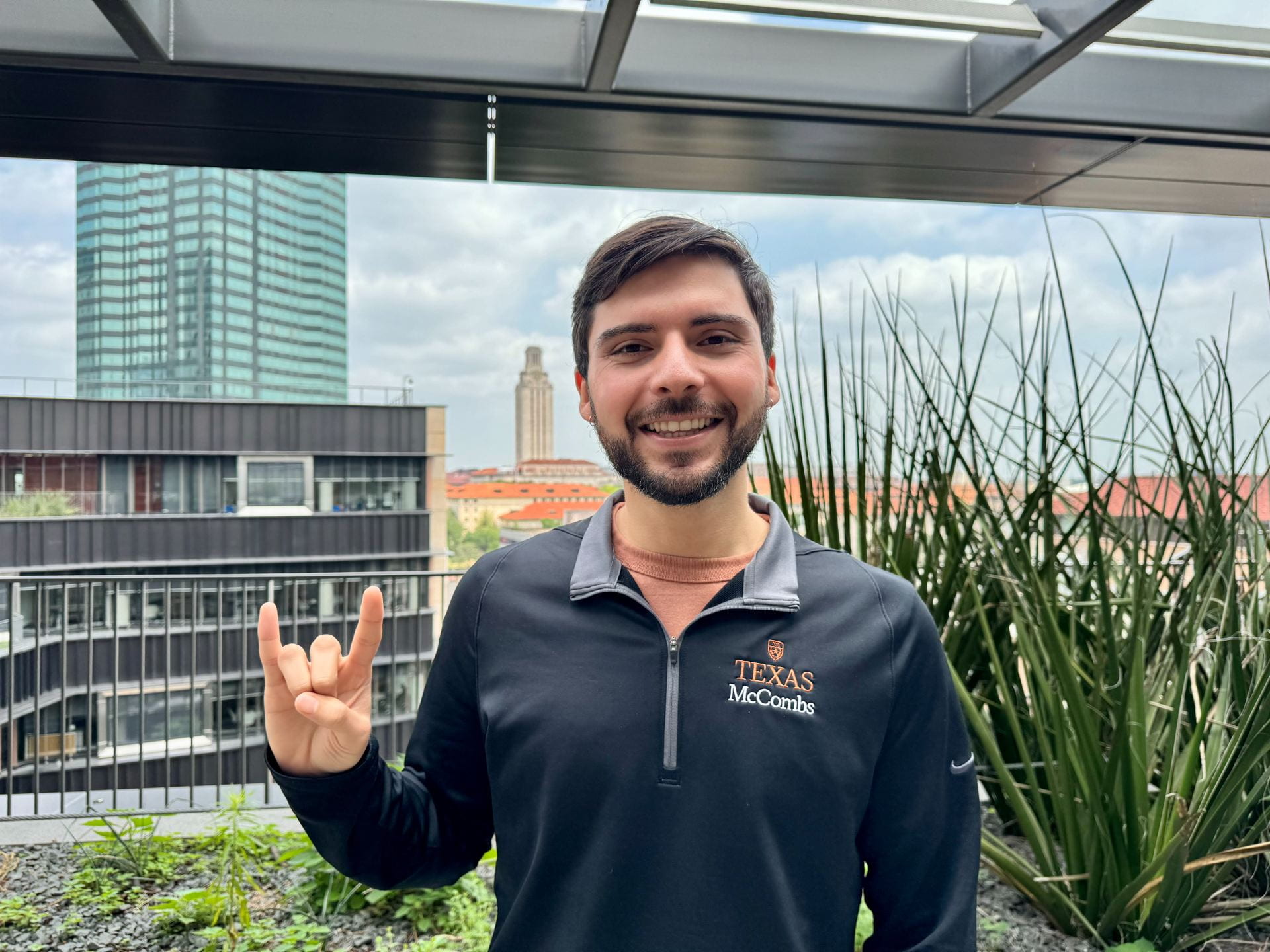 Eric Martinez poses with a Hook 'Em at Rowling Hall with the UT Tower behind him 